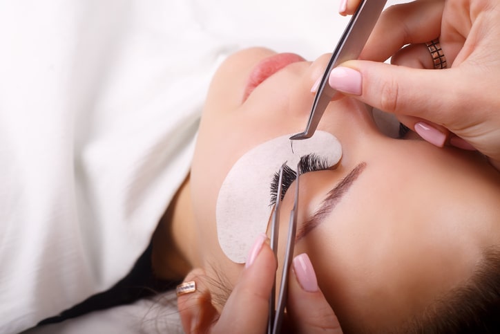 Woman getting eyelash extensions applied in salon